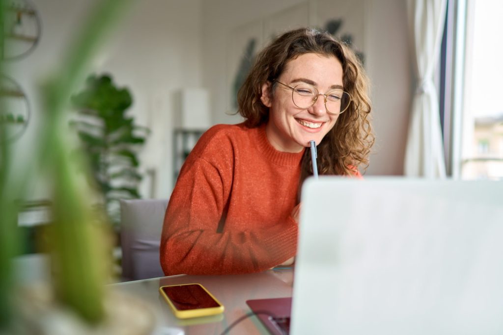 Female student sitting at desk and smiling at laptop